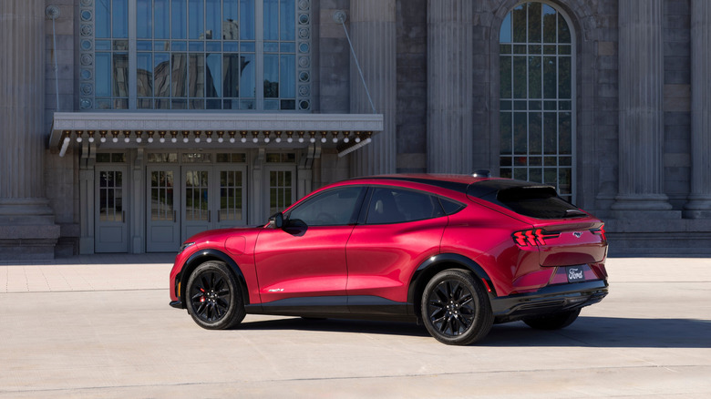 Rear 3/4 view of a red Ford Mustang Mach-E in front of a stone building