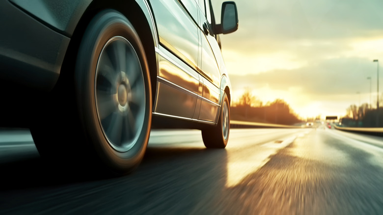 Low angle of a car's tires as it drives down a straight highway at sunset