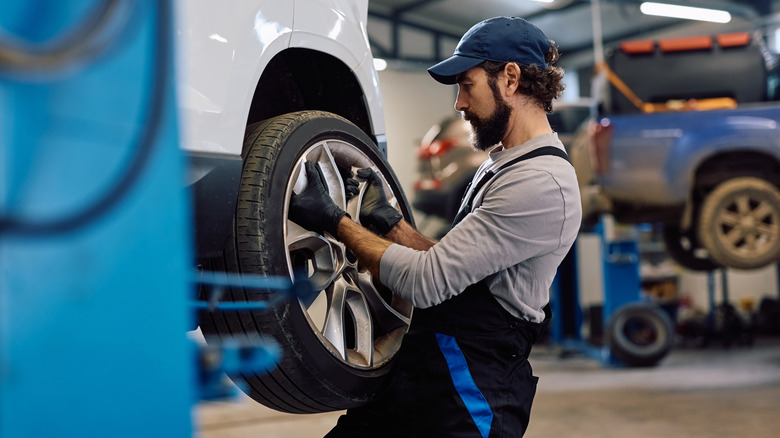 A tire tech removing a wheel from the back of a car up on a lift inside a shop