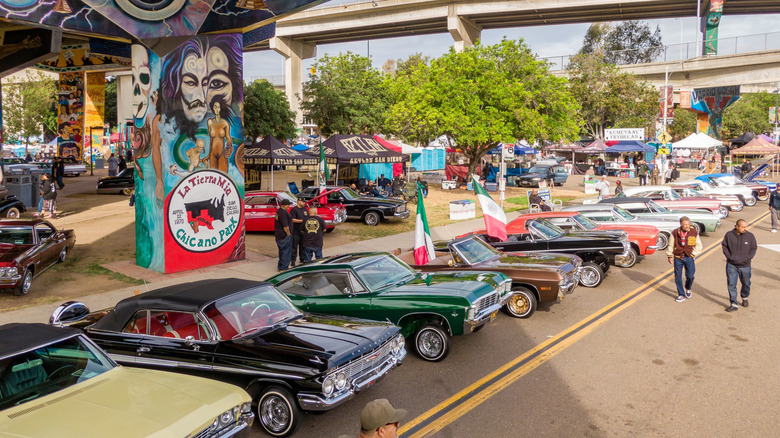 San Diego, California - April 25, 2026: A low-altitude drone view of restored classic cars and lowriders with hoods open for display. Attendees gather under the Coronado Bridge for the 56th Annual Chicano Park Day celebration in Barrio Logan, San Diego.  by: Oak City Drone