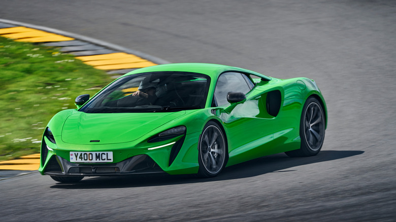 front three-quarters shot of a bright green McLaren Artura driving around a corner on a racetrack pask black-and-yellow curbs and green grass