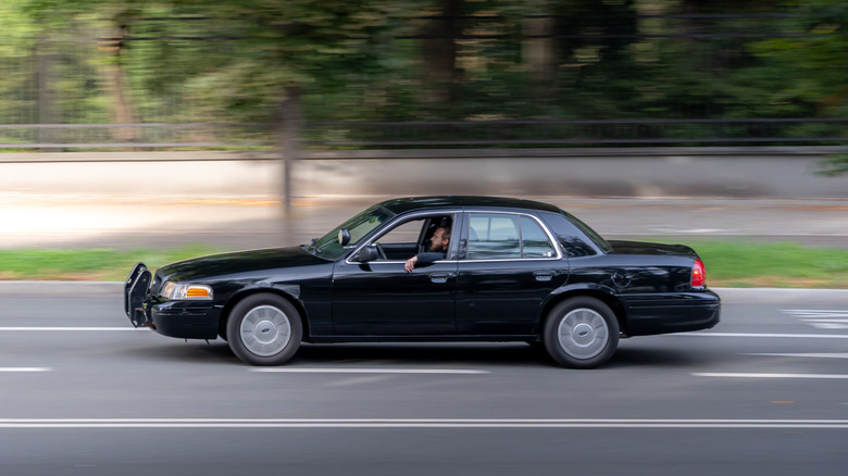 A side shot of a black Ford Crown Victoria being driven on the highway