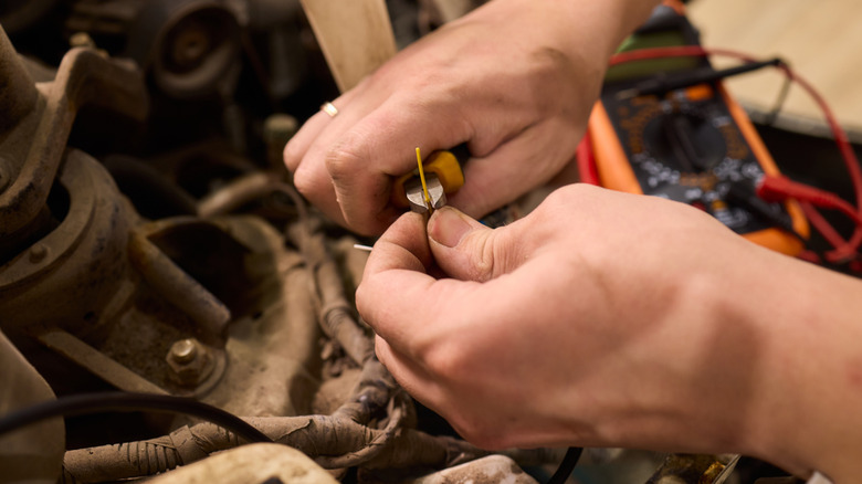 A man stripping wire and using a voltmeter under the hood of the car.