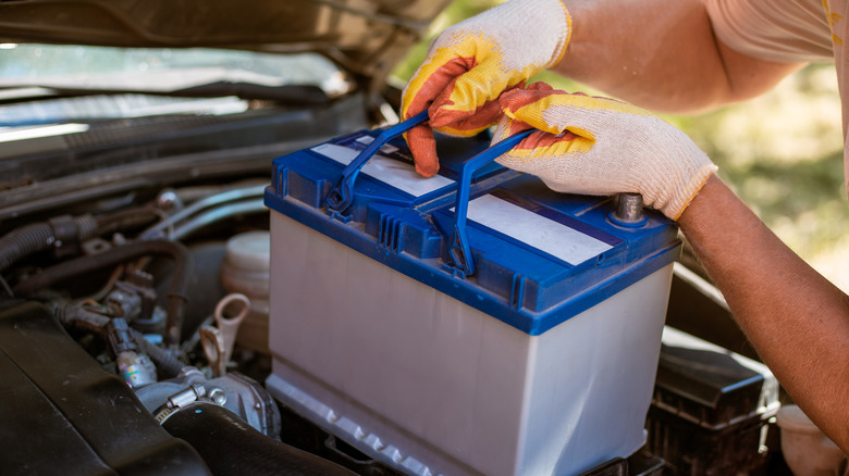 A man inserts a battery under the hood of a car.