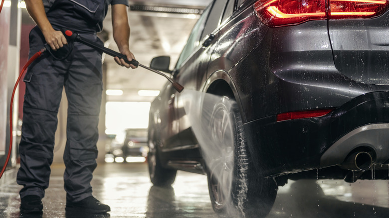 A car wash technician using a pressure washer to rinse the wheels and tires of a small SUV