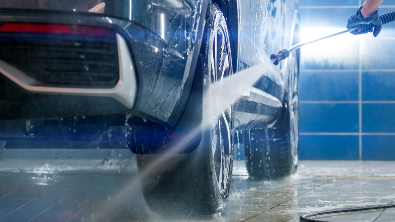 A person using a pressure washer to clean the wheels, tires, and underside of a crossover SUV