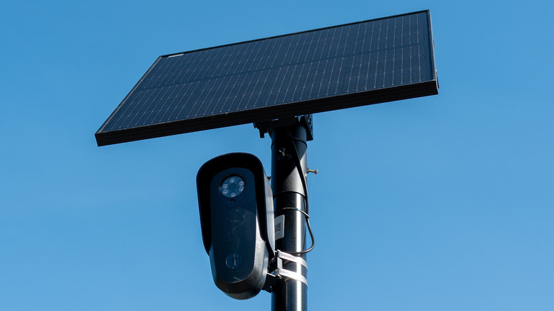 A Flock security camera over a street against a sky blue background.