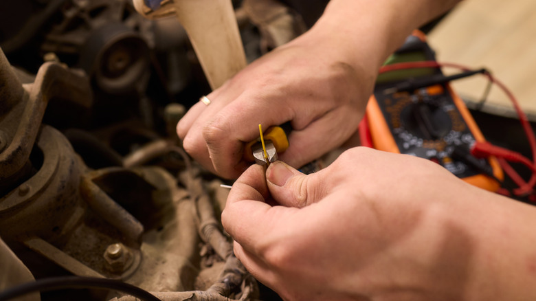 A man stripping wire and using a voltmeter under the hood of the car.