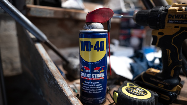 A can of WD-40 stored in garage near a DeWalt power drill and a tape measure