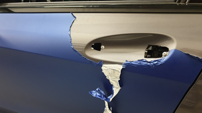 A torn blue car wrap revealing the car's original paint color.
