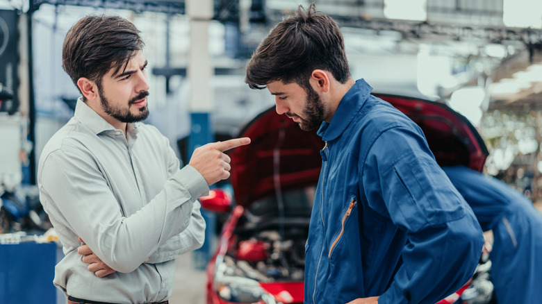 Disgruntled customer arguing with mechanic in front of his car