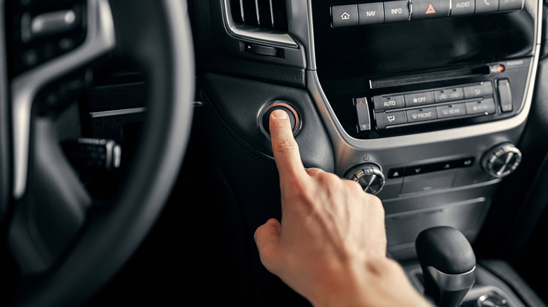 A close-up image of a person's hand pressing a pushbutton start in a modern car