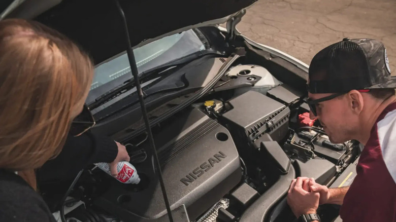 A woman pouring Sea Foam Motor Additive into the engine of a Nissan