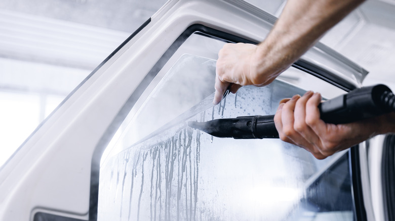 A person using a steamer to remove car rear window tint.