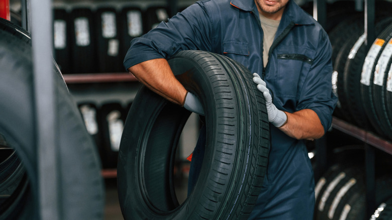 A person carrying a tire in a tire shop.