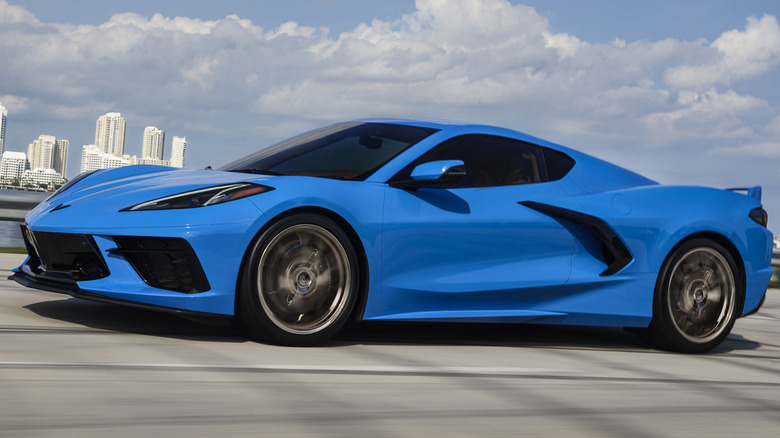 A blue Corvette driving along a body of water.