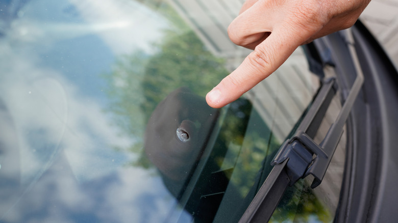 A persons finger pointing to a bullseye type crack in a windshield