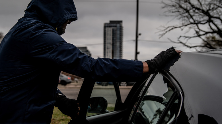 Stock image of a car thief breaking into a car.
