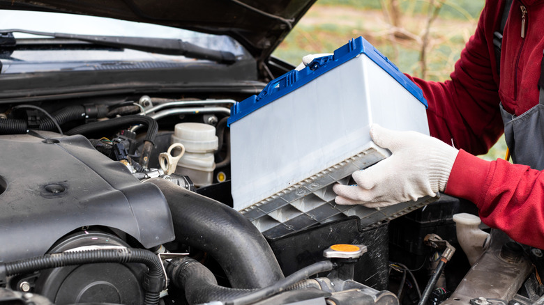 A blue and gray car battery is being installed in an engine bay.