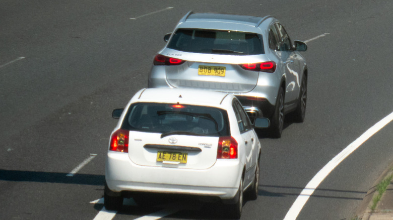 A white subcompact hatchback tailgating a gray crossover on the highway