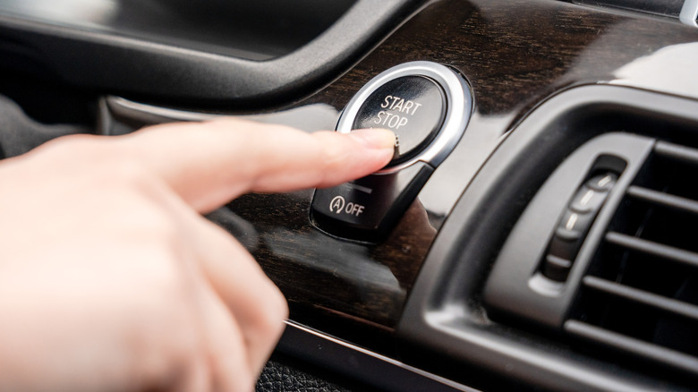 Close-up of a finger pressing an engine start/stop switch on a car dashboard