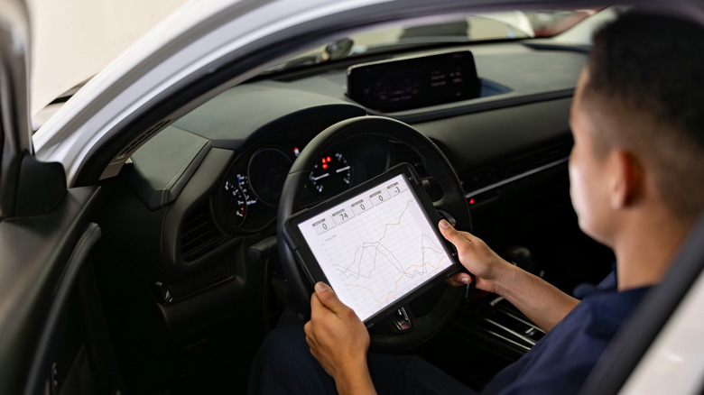An auto tech sitting in the driver's seat of a car looking at a graph of data on a tablet