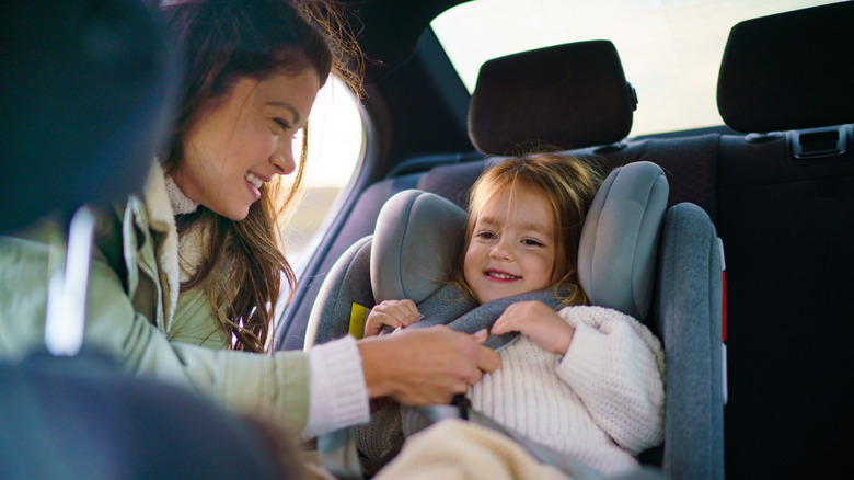 A woman securing a little girl into a child car seat