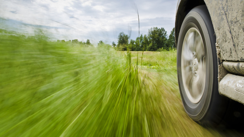 Close up of off-roader wheel from vehicle driving close to high grass