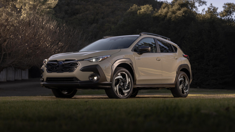 Tan 2026 Subaru Crosstrek Hybriad left front quarter view parked with a tree-covered hill in background