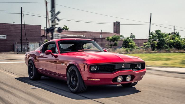 A red Equus Bass 770 with buildings and a meadow in the background