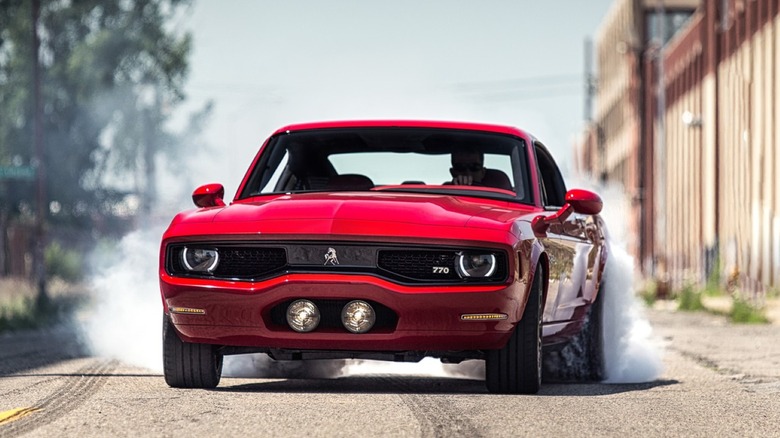 A red Equus Bass 770 boutique muscle car smoking its rear tires on a public street