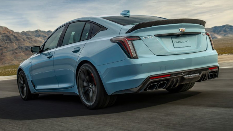 A cyan Cadillac CT5-V Blackwing driving down a road with mountains in the background