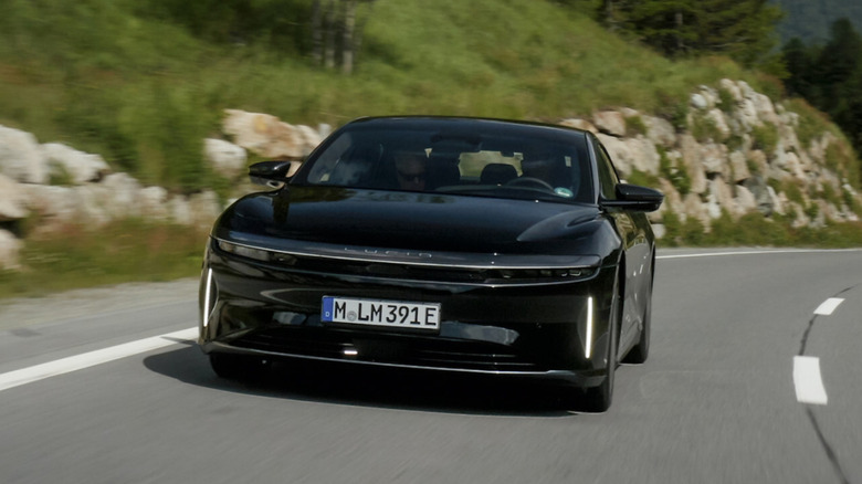 A Lucid Air Grand Touring driving on a road near a grassy hill
