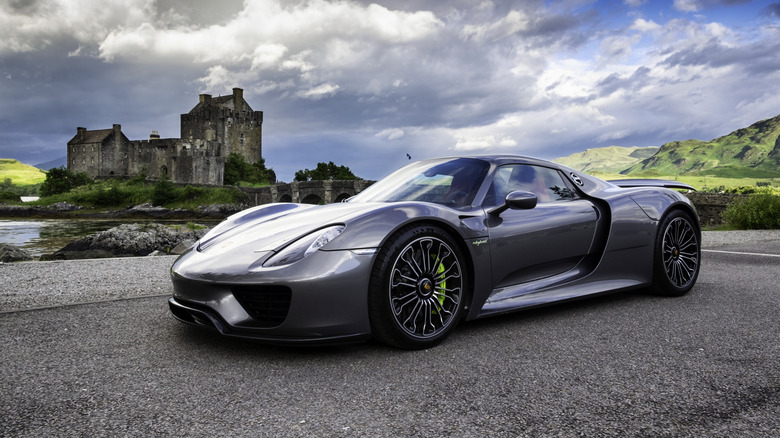 A dark gray Porsche 918 parked in front of a castle