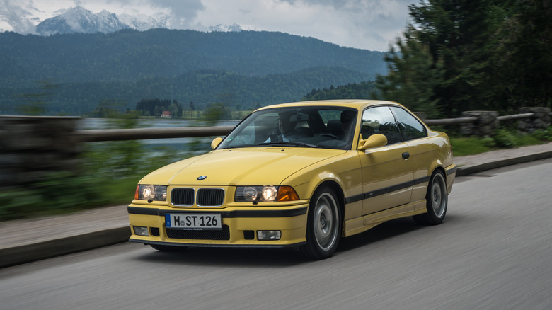 A yellow E36 M3 Coupe driving down a road.