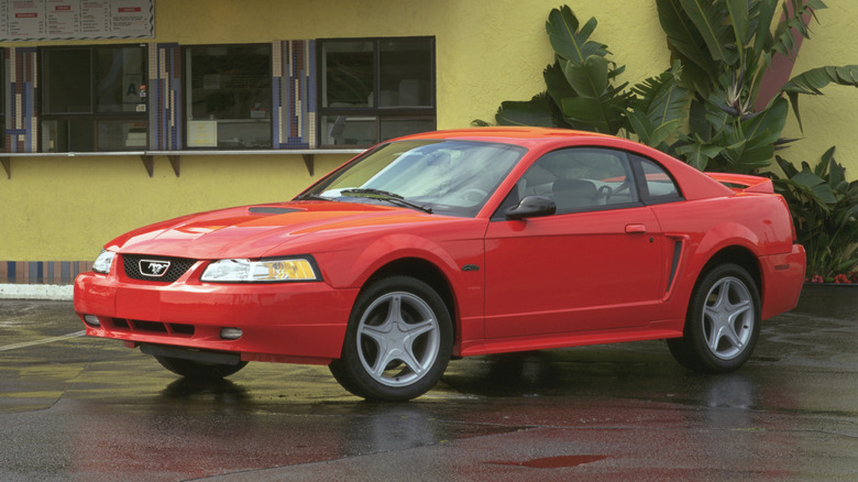 A 2000 Ford Mustang GT Coupe in red outside on wet pavement next to a yellow building.