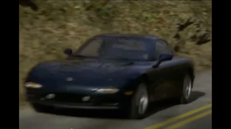 Screenshot showing a black FD RX-7 driving past a brown leaf-covered hillside
