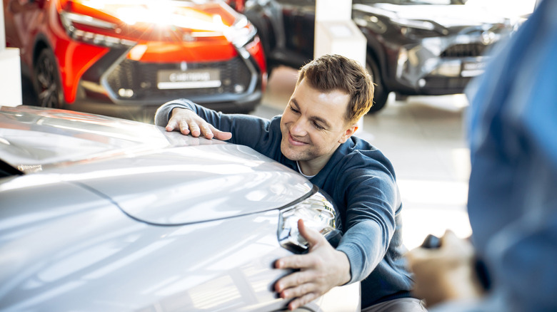 Man hugs the front of a car in a dealership showroom