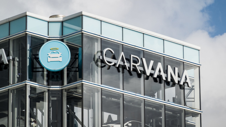 The top part of a Carvana used car tower against a blue sky and clouds.