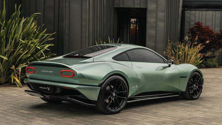 A rear three-quarters shot of the light green Project V parked on bricks in front of a black structure and plants