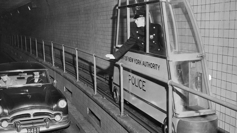 A police officer in a very skinny train car signals to a driver in the Holland Tunnel.