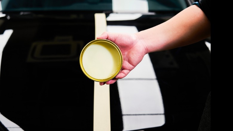 Person shows an open jar of yellow car wax