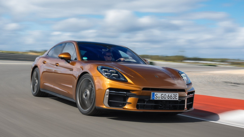 Front three quarters shot of a Madeira Gold Metallic Panamera Turbo S E-Hybrid driving around the corner of a race track