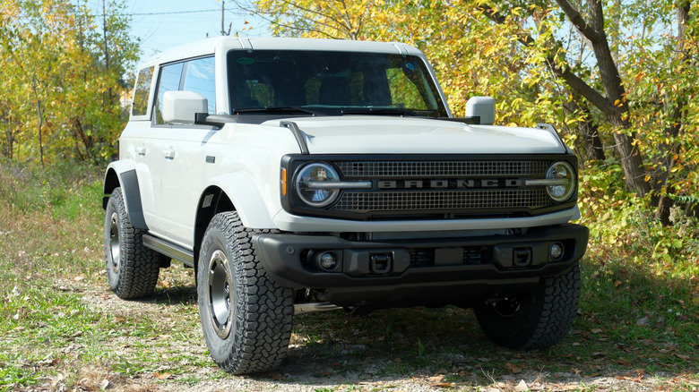 A white Ford Bronco is shot from the front in pleasant woods.