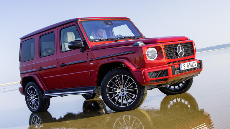 A red Mercedes-Benz G-Class parked in very shallow water on what appears to be a salt flat