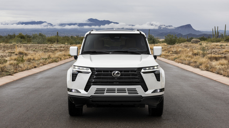 A white Lexus GX is photographed from the front against a mountain backdrop.