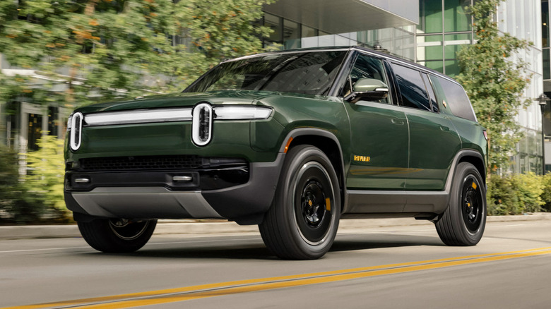 A green Rivian R1S drives down a city street.