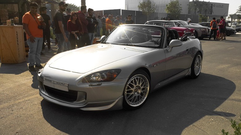 A silver Honda S2000 AP2 drives past a small group of people