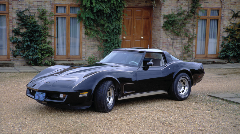 Image a black 1980 C3 Corvette taken outside in front of a building.