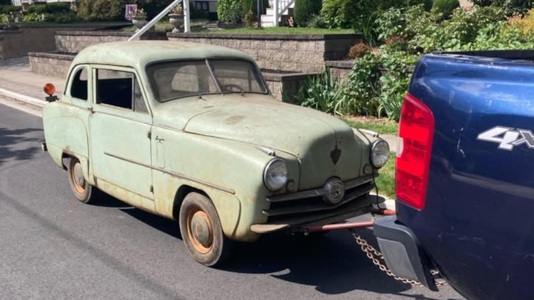 A rusty green Crosley coupe behind a pickup